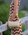 Person wearing a colorful dress holding The Lachlan raffia bag with gold stud accents
